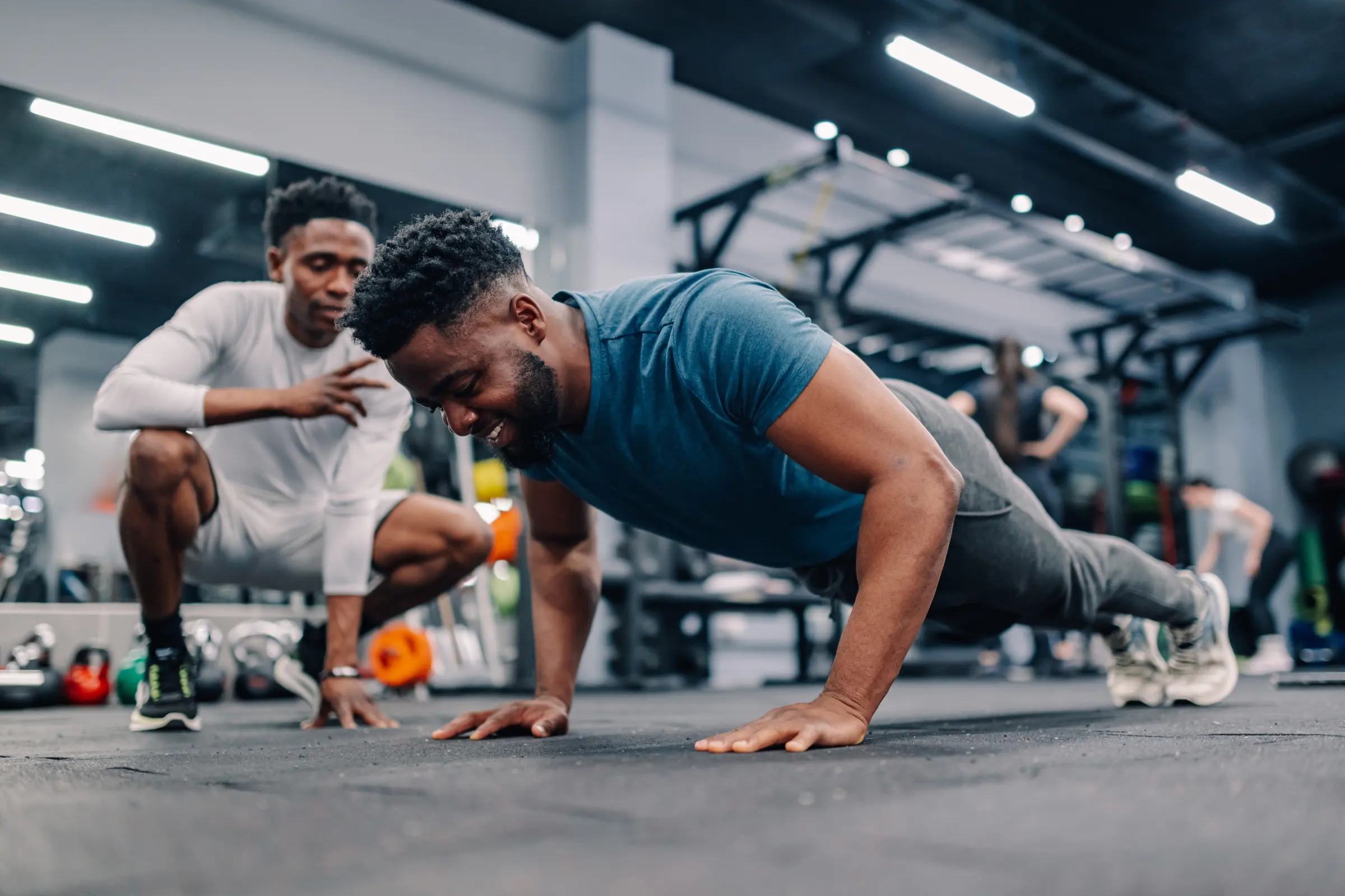 A coach crouched beside an athlete, watching his push-up